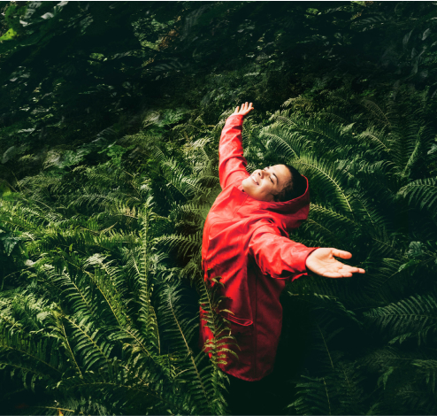 Mujer en el bosque con los brazos abiertos, sonriendo hacia el cielo