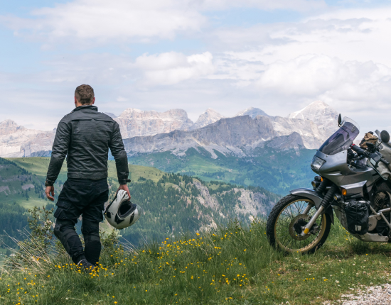 Motociclista en las montañas, junto a su motocicleta y con el casco en su mano