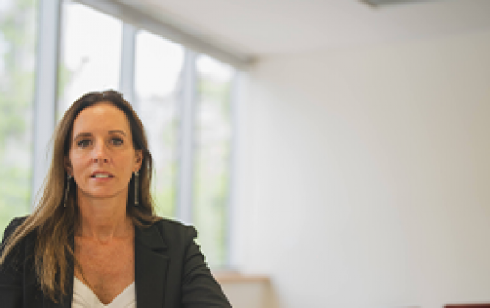 La gerenta de APV de LarrainVial, Claudia Ovalle, sentada ante una mesa blanca y mirando a cámara.